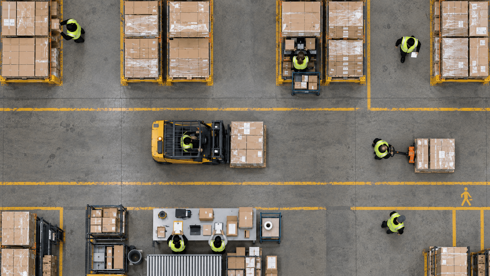Overhead warehouse with workers, a forklift, pallet racks, and a packing station